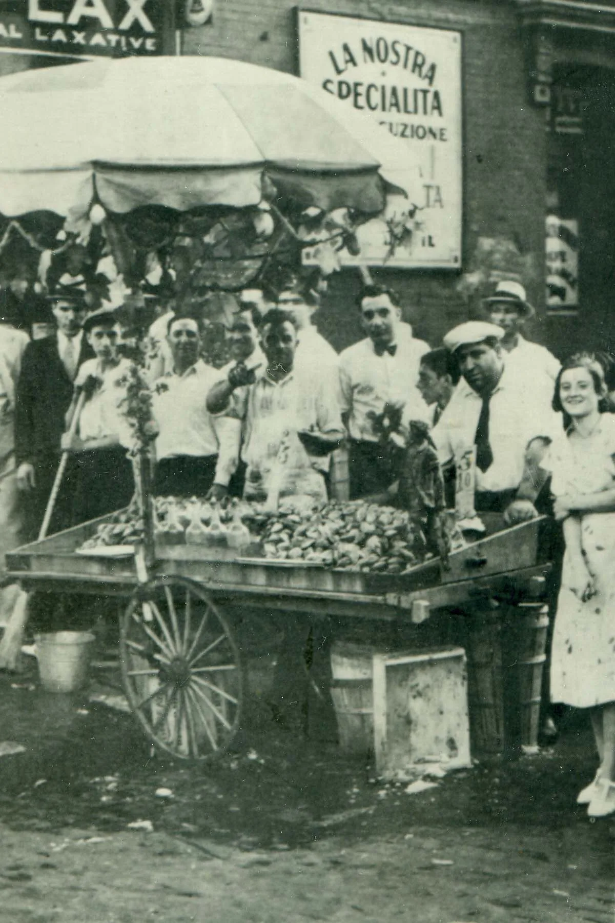 An Italian food pushcart surrounded by a crowd on a New York City street in the 1930s.
