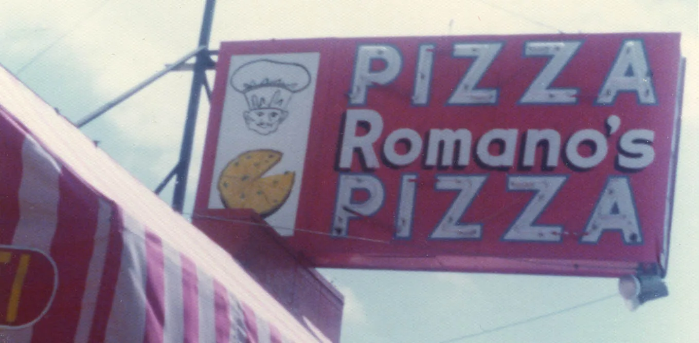 The original painted Romano's Pizza sign in red and white, with a chef's face and a pizza.